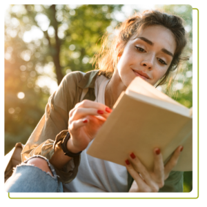 Image of young woman smiling and reading book in green park